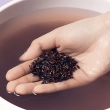 Hand holding black rice grains over a bowl of water