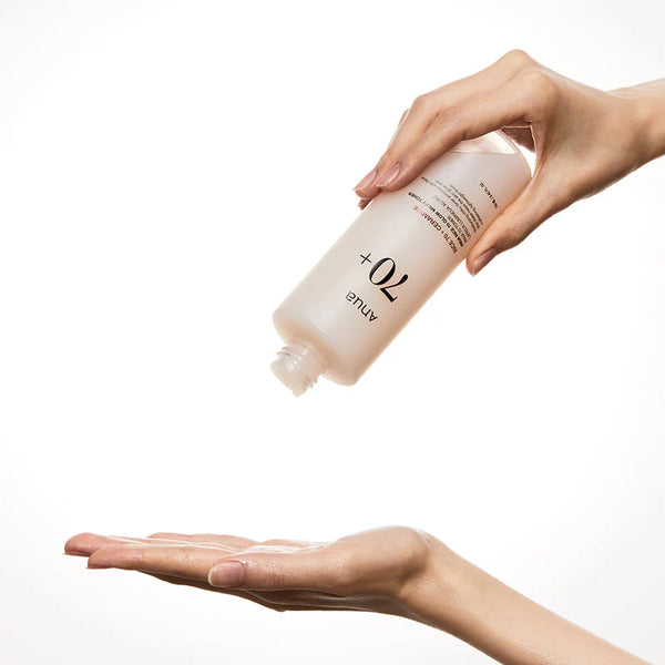 Hand holding a bottle of skincare product over another hand with visible cream on the palm.