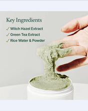 Hand holding green clay paste above a container with text listing key ingredients.
